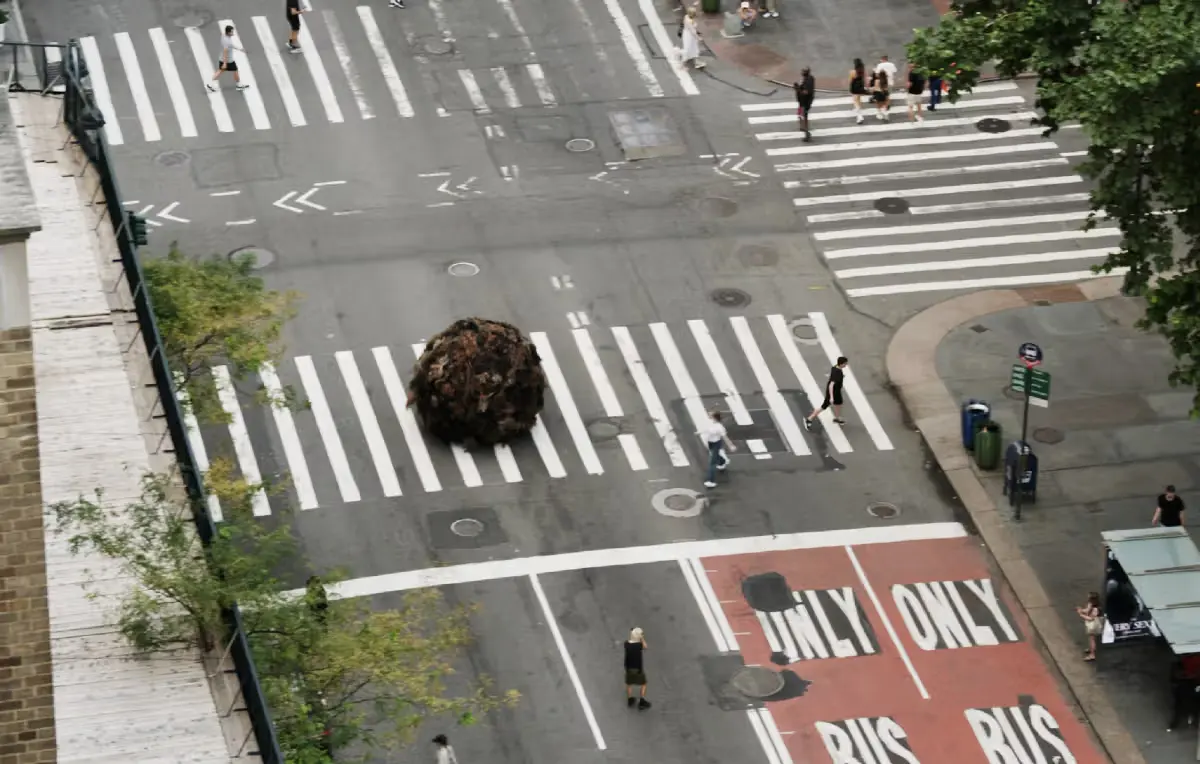 Aerial view of K18's giant "Tumblehair" installation sitting in a New York City crosswalk, with pedestrians crossing the street around it and a bus-only lane visible nearby.